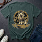 A blue spruce graphic t-shirt laid flat on a dark slate background, styled with a pair of blue jeans, white sneakers, and a coiled rope. The back of the shirt features a large circular graphic of a Chinese Crested dog inside a compass design with the text 'GOT YOUR 6' below it.